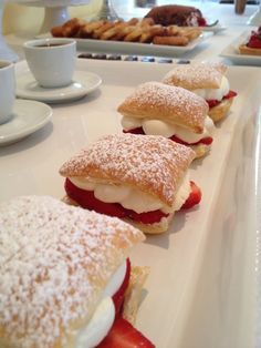 pastries are lined up on a long white plate with strawberries and powdered sugar