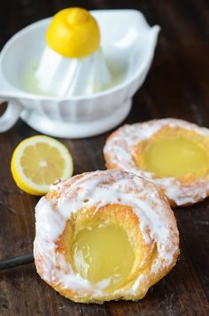 two lemon filled donuts on a wooden table next to a white bowl with lemons