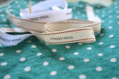 two white ribbons with happy stitch on them sitting on a green polka dot tablecloth