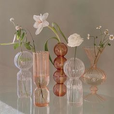 several vases with flowers in them sitting on a glass table top next to each other