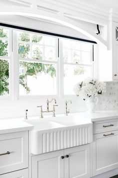 a white kitchen with two sinks and a window in the backround above it