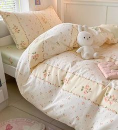 a white bed with pink and green floral comforter, pillows and a stuffed animal