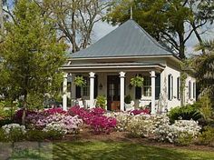 a small white house surrounded by flowers and trees