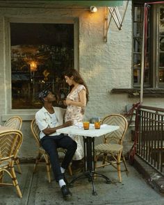 a man and woman sitting at an outdoor cafe table with drinks in front of them