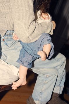 a woman holding a baby in her arms on top of a wooden floor next to a chair