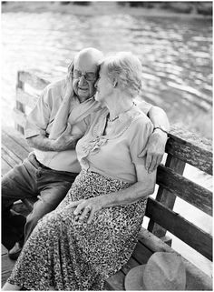 an older man and woman sitting on a bench next to each other by the water