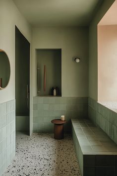 an empty bathroom with green tile walls and white tiles on the floor, along with a bench