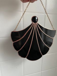 a hand holding a black and gold shell shaped pendant on a chain hanging from a white tile wall