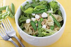 a white bowl filled with pasta salad and green beans on top of a yellow table