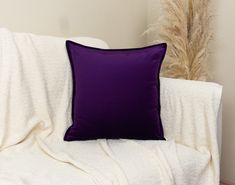 a purple pillow sitting on top of a white couch next to a tall grass plant