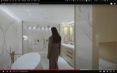 a woman standing in a bathroom next to a bathtub and sink with the door open