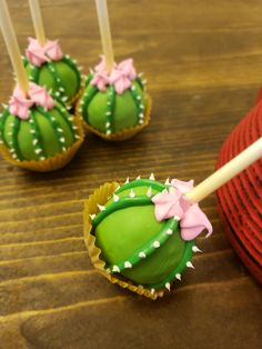 some green cake pops with pink bows on them sitting on a wooden table next to a straw hat