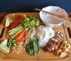 a wooden cutting board topped with meat and veggies next to a bowl of dipping sauce