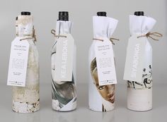 three empty wine bottles wrapped in paper with tags tied around the top and bottom one has an image of a woman's face on it