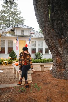 a woman sitting on a bench in front of a house with an american flag hanging from the tree