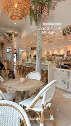 the inside of a restaurant with white wicker chairs and round wooden table surrounded by hanging plants