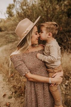 a woman holding a small child in her arms while wearing a cowboy hat and dress