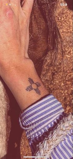 a woman's hand with a cross tattoo on her left wrist and the other hand holding a cell phone