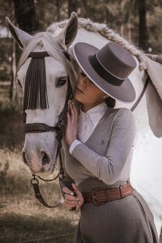 a woman wearing a hat hugging a white horse