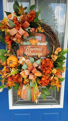 a wreath with pumpkins and leaves is hanging on the front door's blue door