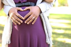 a pregnant woman holding her belly in the shape of a heart with her hands on her stomach