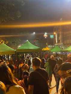 many people are walking around in the street at night with green tents on either side