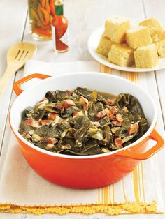 a bowl filled with collard greens on top of a table next to plates of food