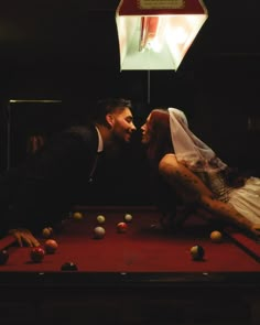 a bride and groom playing pool together in a dark room with balls on the table