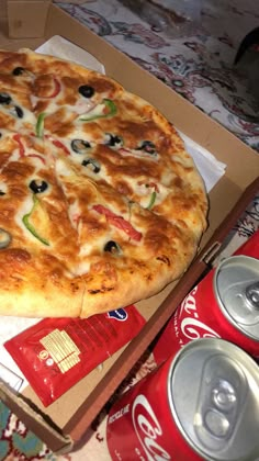 a pizza in a box next to cans of soda