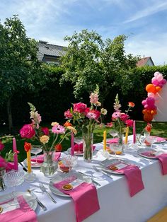 the table is set with pink and orange flowers, candles, plates and napkins