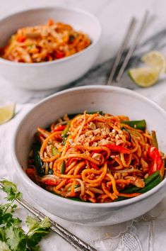 two bowls filled with noodles and vegetables next to some chopsticks on the table