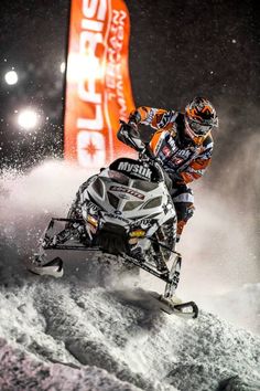 a man riding on the back of a snowmobile down a snowy slope at night