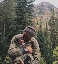 a man and woman hug each other in front of some trees with mountains in the background