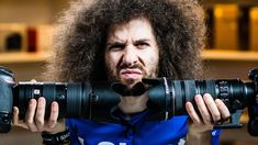 a man with long hair holding two camera lens's in front of his face