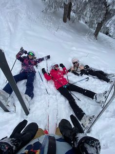 three people laying in the snow with skis on their feet and one person holding two ski poles