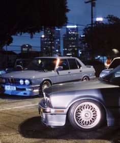 two cars parked next to each other in a parking lot with buildings in the background