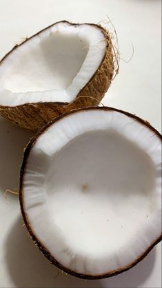 two whole coconuts sitting next to each other on a white counter top with one cut in half