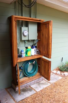 an open wooden box on the side of a house with hoses and other items in it