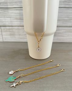 the initial charm necklace is on display next to a cup