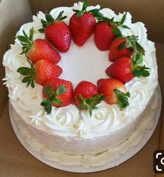 a cake with white frosting and fresh strawberries on top in a cardboard box