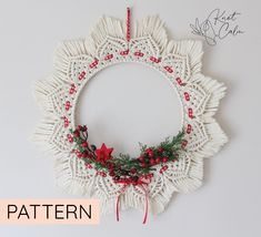 a crocheted christmas wreath hanging on the wall with red berries and pine cones