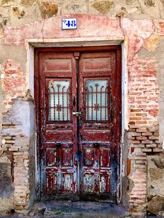 an old red door with two windows on the side of a brick building in italy