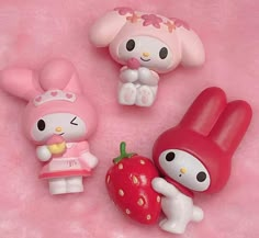 hello kitty toys are laying on a pink surface with an apple, strawberry and bunny