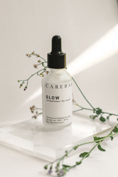 a bottle of carebar glow next to some flowers on a white surface with light coming from behind it