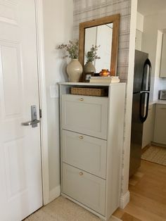 a white cabinet sitting in the corner of a room next to a door with a mirror on it