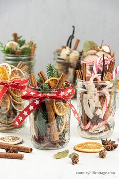 three jars filled with cinnamons, orange slices and star anise on top of a table