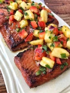 two pieces of steak with pineapple salsa on top and another piece of meat in the background