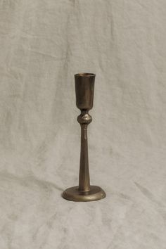 a small metal candle holder sitting on top of a white tablecloth covered floor next to a wall