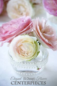 three pink and white flowers in a glass vase with pearls around the edges on a table