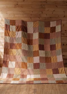 a large brown and tan quilt sitting on top of a wooden floor next to a window